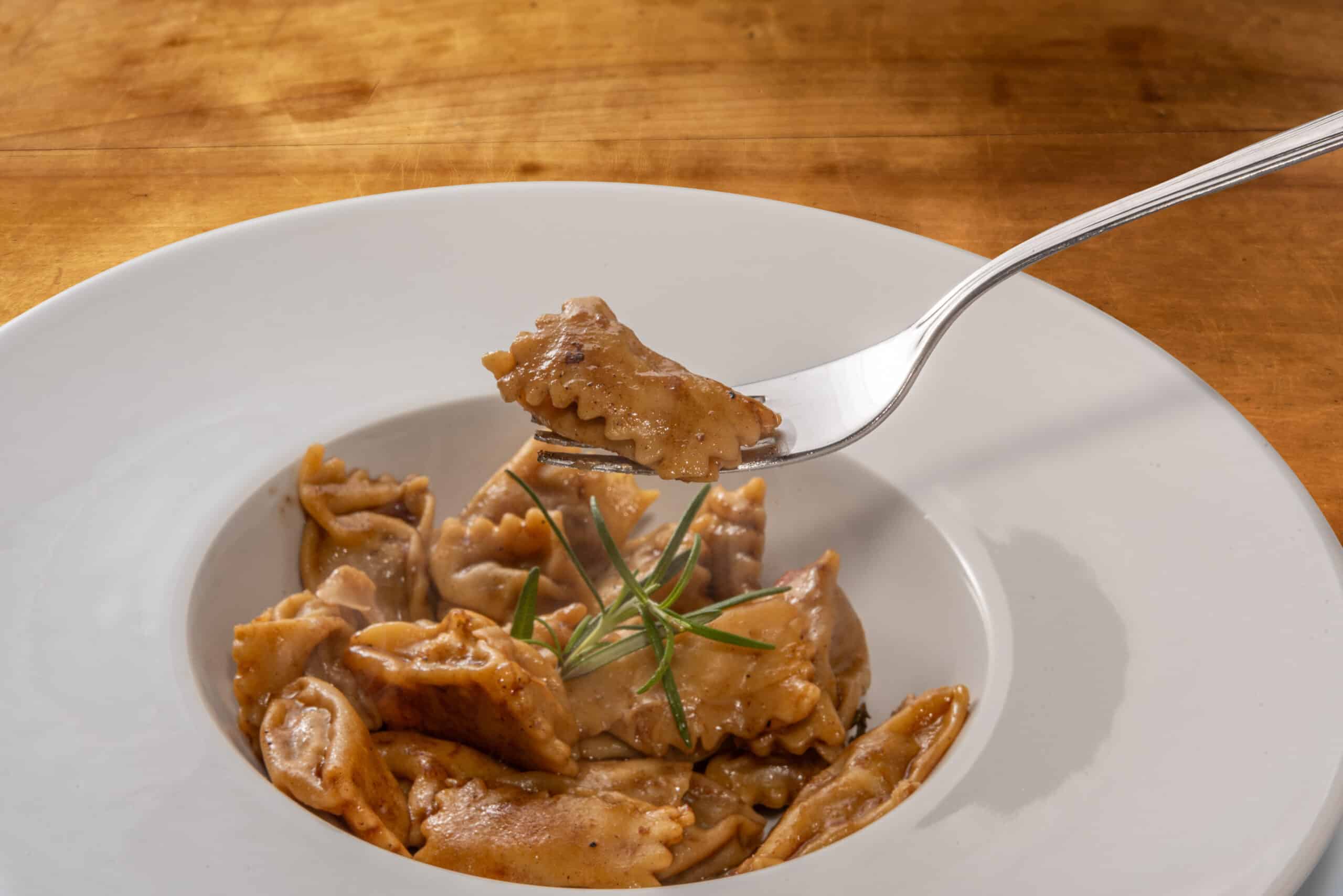 Agnolotti del Plin served with roast sauce, Plin egg pasta ravioli over fork on white plate on wooden table